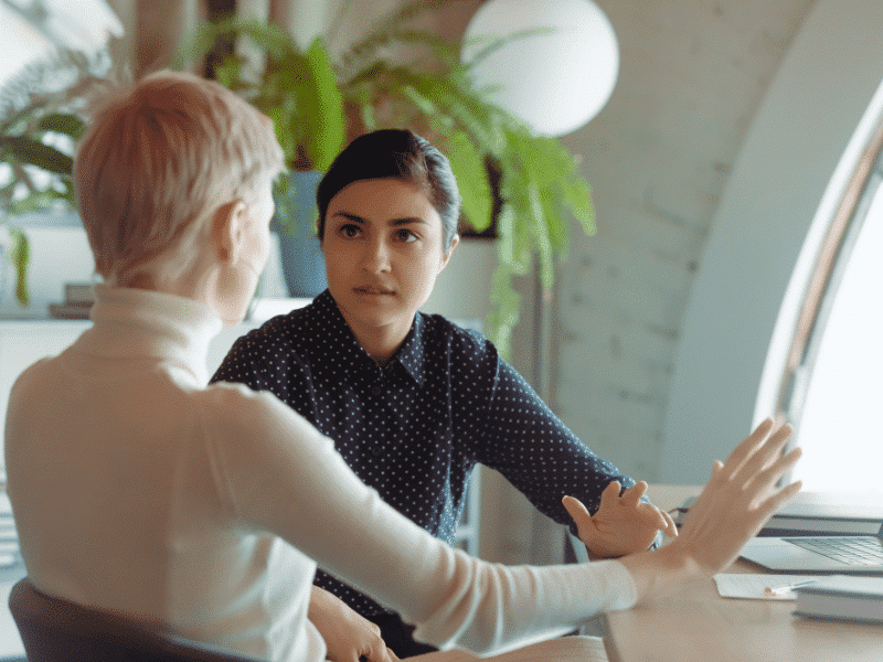 Indian and caucasian businesswomen negotiating sit at desk in office stock photo