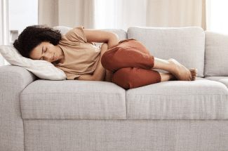 Woman curled up on couch in pain holding her pelvic area